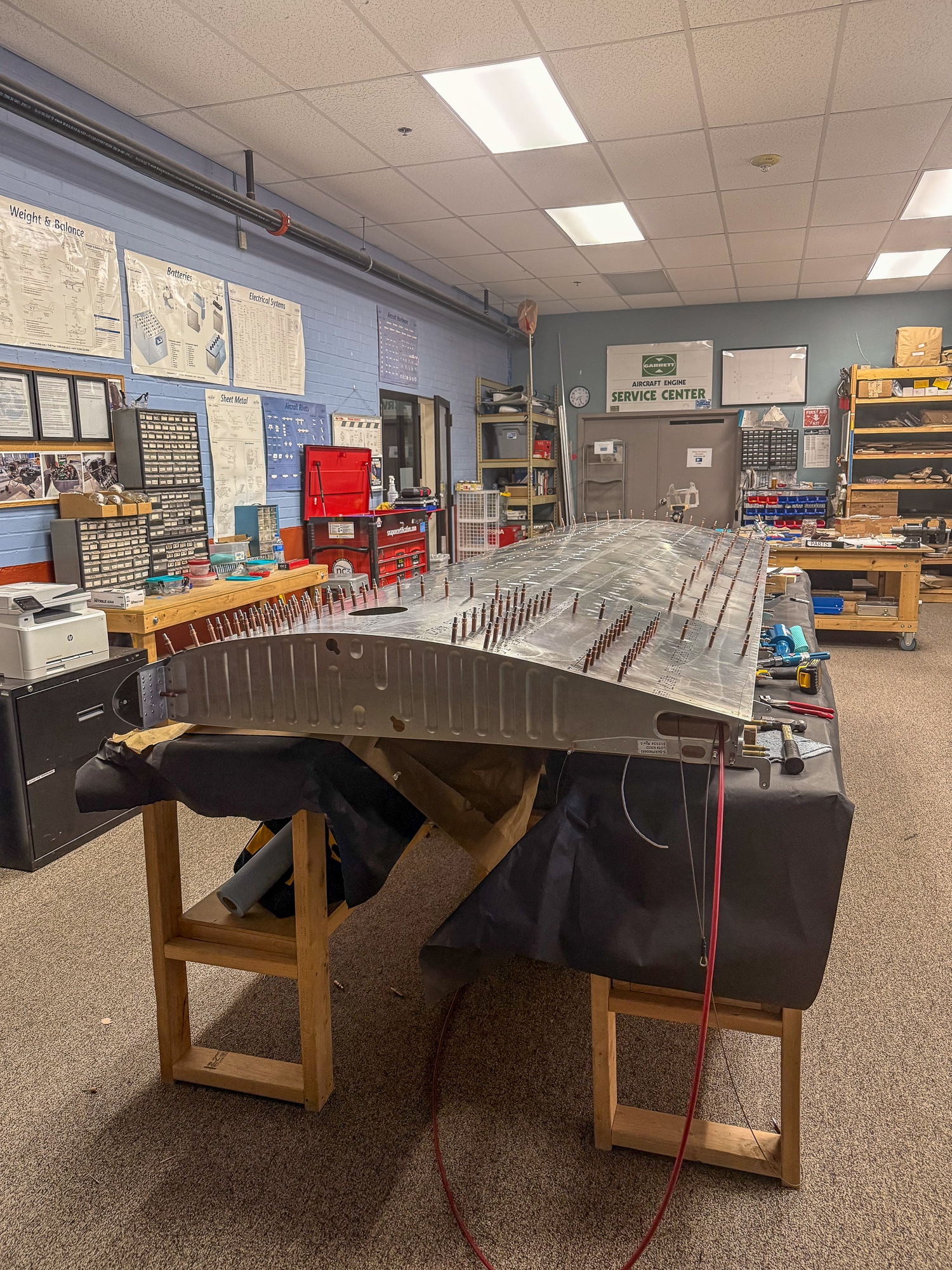 A model of an airplane wing cross-section, resting on a long bench in a workroom.
